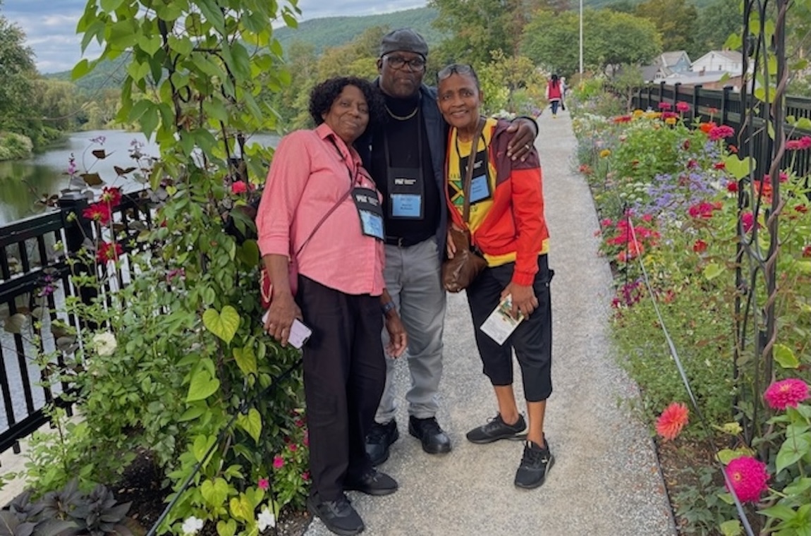 Three people smile with arms around one another as they stand under a vine-covered arch on the Bridge of Flowers